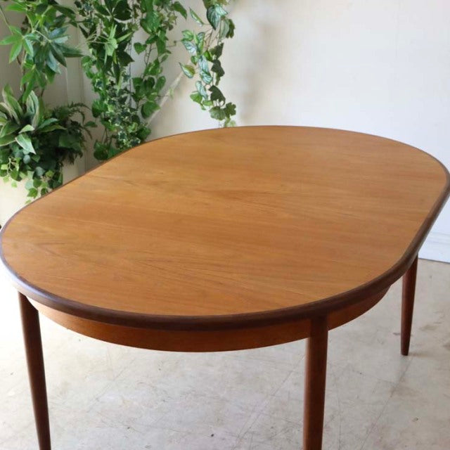 Oval vintage teak dining table with rounded edges, slender tapered legs, mid-century British-Danish design.