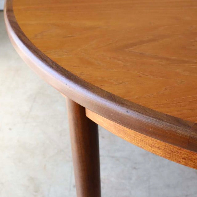 Oval vintage teak dining table corner showing rich wood grain and rounded edge with round tapered legs, British mid-century.