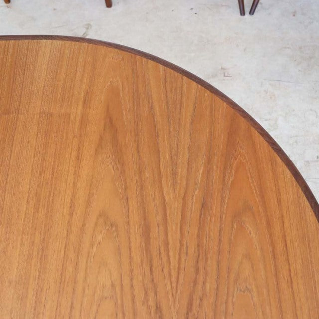 Oval vintage teak dining table top showing smooth wood grain with tapered mid-century British design legs visible in the.