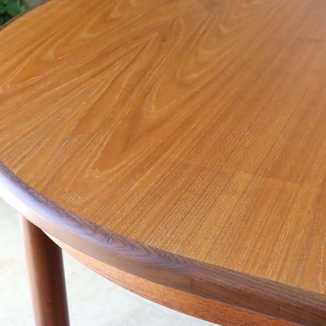 Vintage British mid-century teak dining table with smooth oval top and rounded edges, visible wood grain, and tapered legs,.