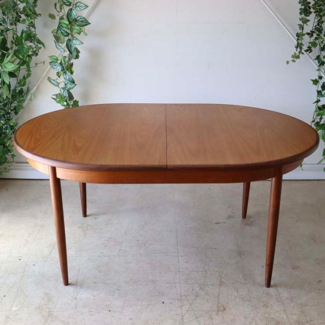 Vintage mid-century British G-Plan teak dining table with oval top and tapered legs, smooth wood grain finish.