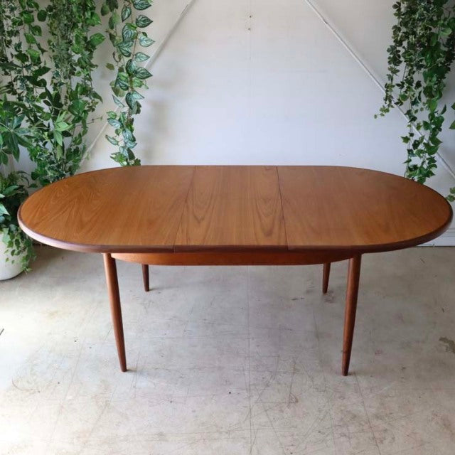 Oval teak dining table with smooth wood grain, slender tapered legs, mid-century British vintage design.