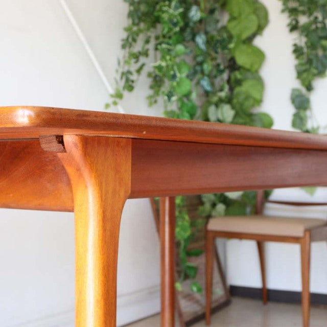 Vintage mid-century British McIntosh teak dining table with smooth wood grain, rounded edges, and slender tapered legs.