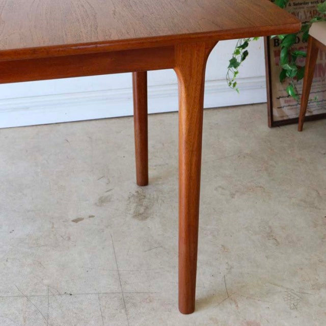 Mid-century British vintage teak dining table corner with tapered rounded leg showcasing natural wood grain and smooth finish.