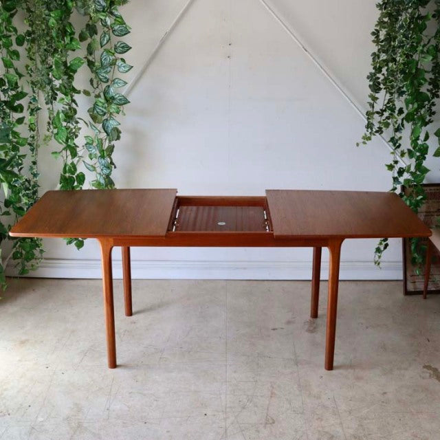 Mid-century British McIntosh dining table in teak with extendable top, showcasing rich wood grain and slender tapered legs.