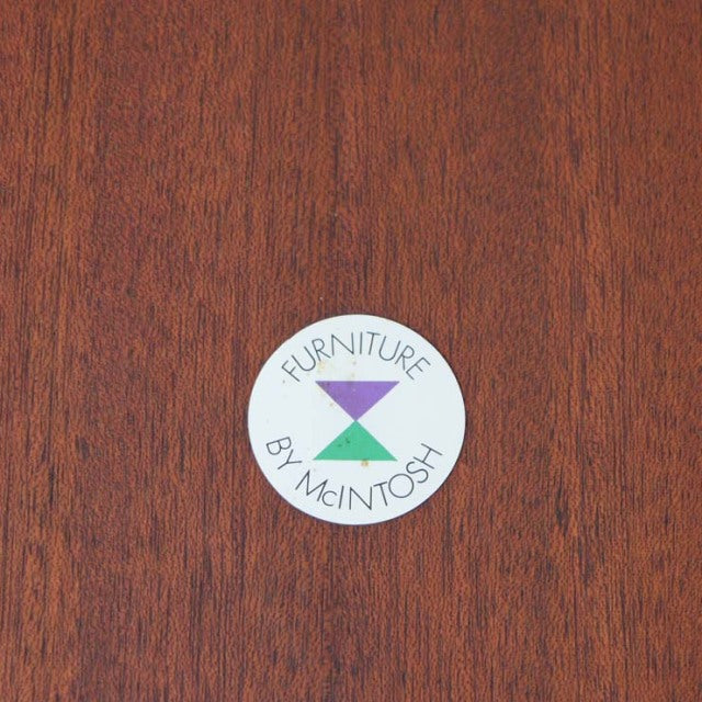 Close-up of rich teak wood grain with smooth finish and circular McIntosh furniture brand label in purple and green vintage.