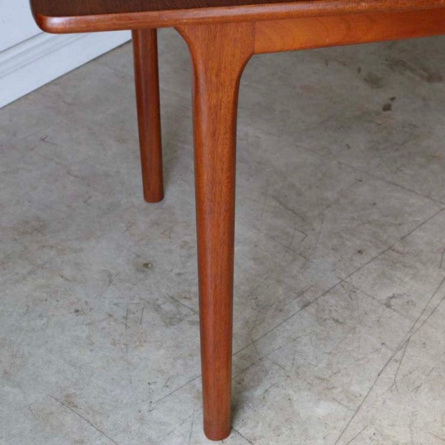 Mid-century teak dining table leg by British brand McIntosh, smooth wood grain, rounded edges, and tapered cylindrical leg.