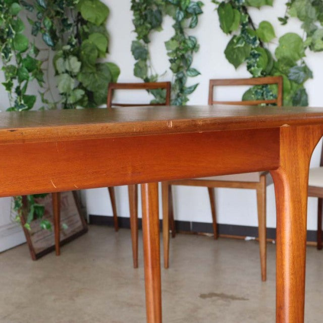 Vintage British mid-century teak dining table with smooth wood grain and slender tapered legs.