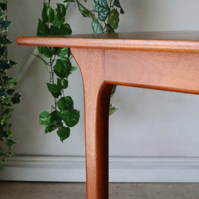 Vintage teak dining table corner with smooth rounded edges, tapered leg, and visible wood grain from British mid-century.