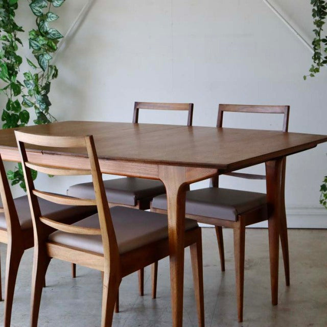 Mid-century British vintage teak dining table with tapered legs and sleek wood grain, paired with matching teak chairs with.