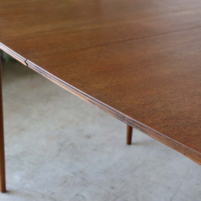 Mid-century British vintage teak dining table with smooth wood grain and slender tapered legs.