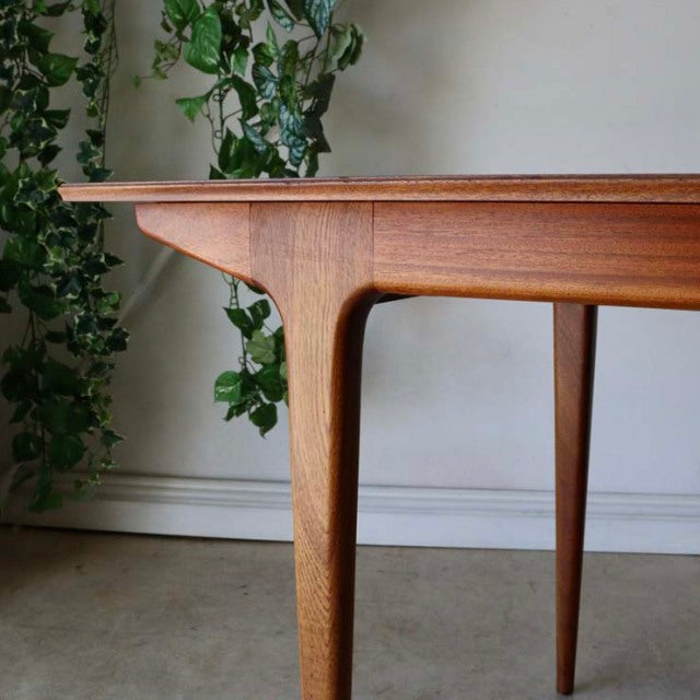 Mid-century British vintage teak dining table with smooth wood grain, tapered legs, and rectangular form.