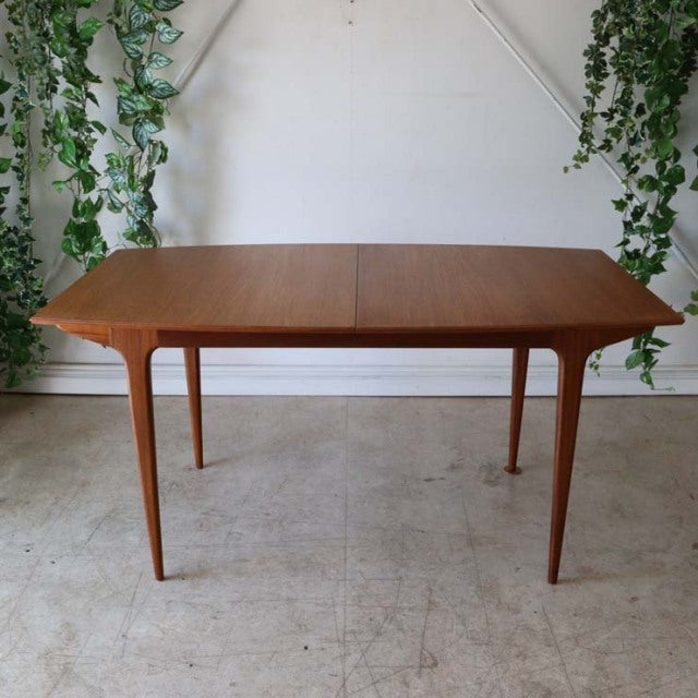 Vintage British mid-century teak dining table with sleek tapered legs and smooth wood grain.