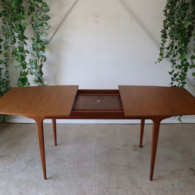 Vintage mid-century British McIntosh dining table in teak with smooth grain and slender tapered legs, featuring an extending .