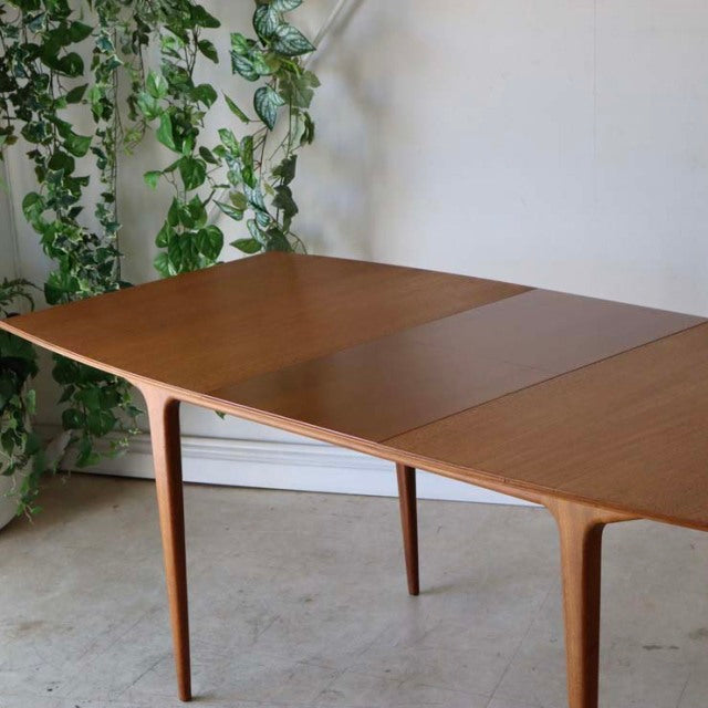 Vintage teak McIntosh dining table with mid-century British design, smooth wood grain, and slender tapered legs.