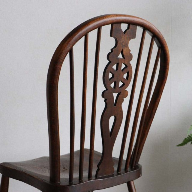 Vintage British teak kitchen chair with curved spindle back, intricate carved central splat, and smooth polished wood grain, .