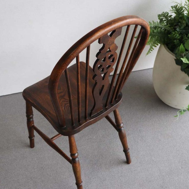 Vintage teak mid-century British kitchen chair with decorative carved splat and spindle back legs on gray floor next to.