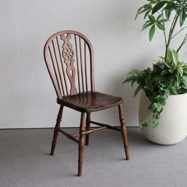 Vintage British teak kitchen chair with mid-century spindle back and carved floral detail, turned legs, and rich wood grain.