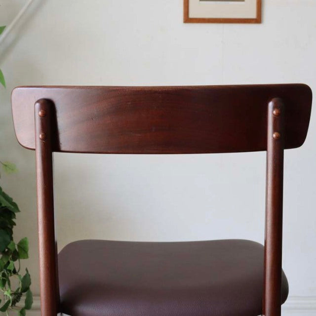 Mid-century British vintage dining chair in teak with a curved rectangular backrest and tapered legs, smooth dark wood grain .