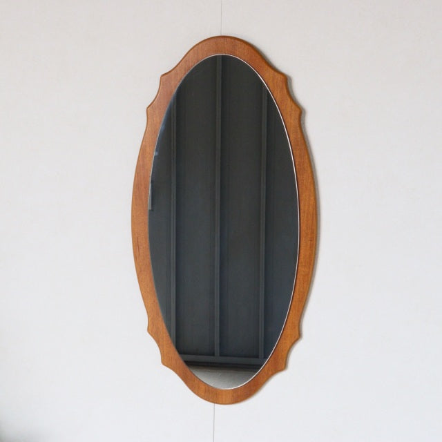Vintage mid-century British teak wall mirror with oval frame and subtle scalloped edges, smooth wood grain visible.