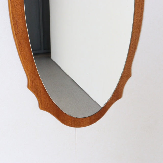 Vintage mid-century British teak wall mirror with oval shape and subtle scalloped edges, showcasing warm wood grain and.
