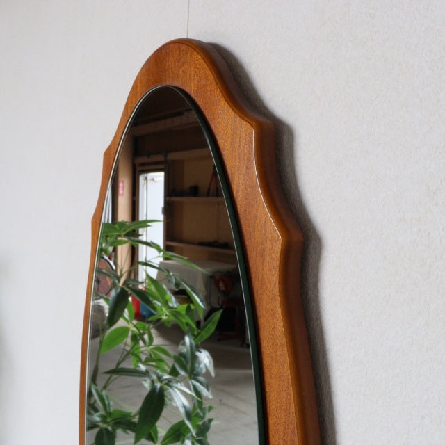 Vintage mid-century British teak wall mirror with an oval shape and smooth, curved edges, showcasing rich wood grain and.