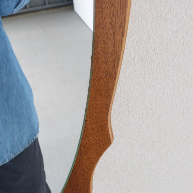 Vintage British mid-century teak wall mirror with elegant oval shape and rich wood grain detailing.