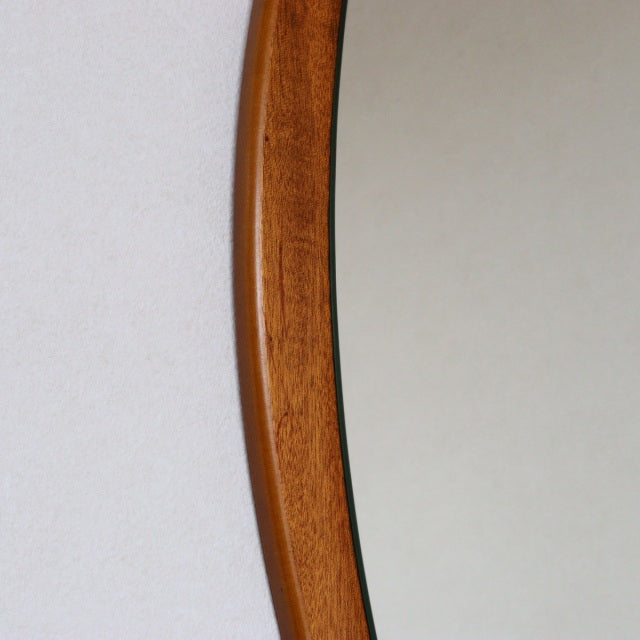 Oval mid-century British vintage teak wall mirror with smooth wood grain frame and minimalist design.