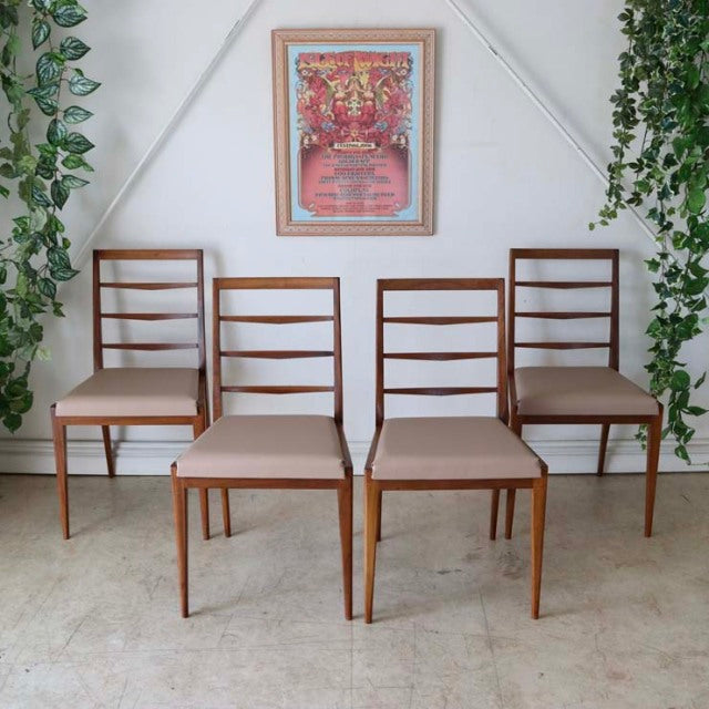 Set of four vintage mid-century teak dining chairs with ladder backs, slender tapered legs, and beige upholstered seats,.