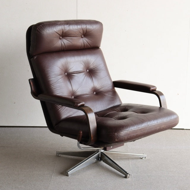 Vintage mid-century armchair with rich brown tufted leather upholstery, teak wood frame, and sleek angled armrests on a.