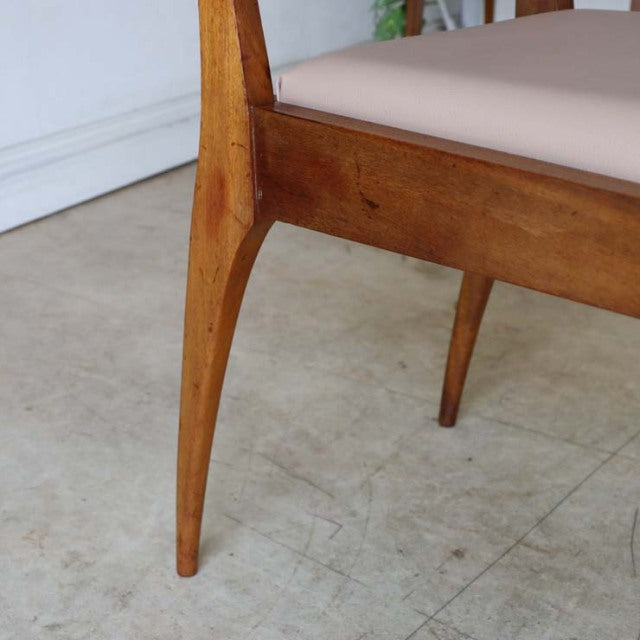 Close-up of mid-century British vintage teak dining chair leg with visible wood grain and tapered design, beige upholstered.