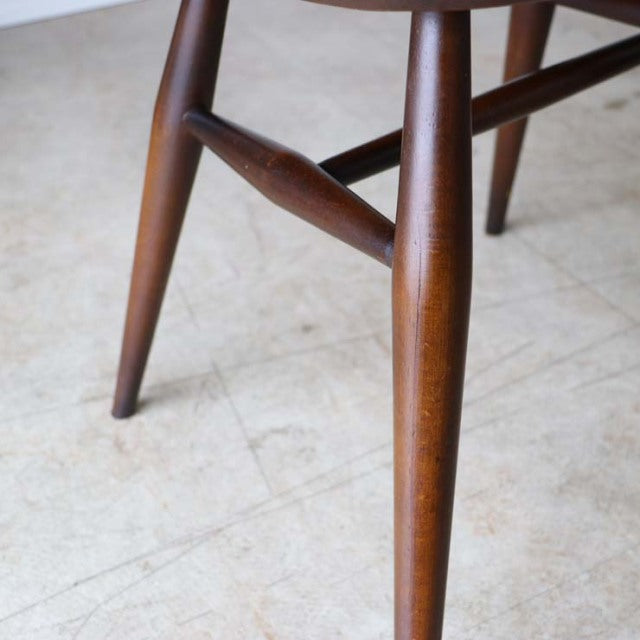 Mid-century British ERCOL Goldsmith highback chair legs in warm teak with smooth grain and tapered form on light floor.