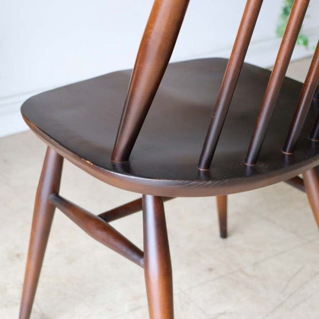 Vintage British mid-century teak dining chair with spindle back and rounded edges, smooth wood grain visible.
