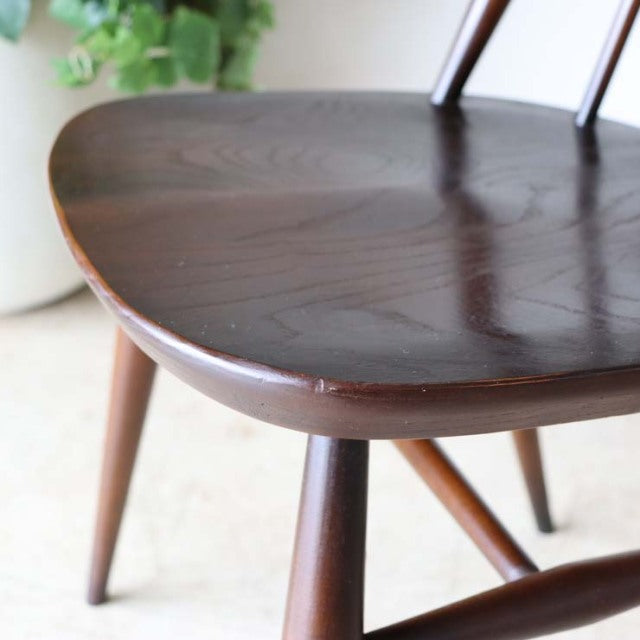 Close-up of vintage ERCOL Goldsmith highback chair seat and tapered teak legs showcasing rich wood grain and mid-century.