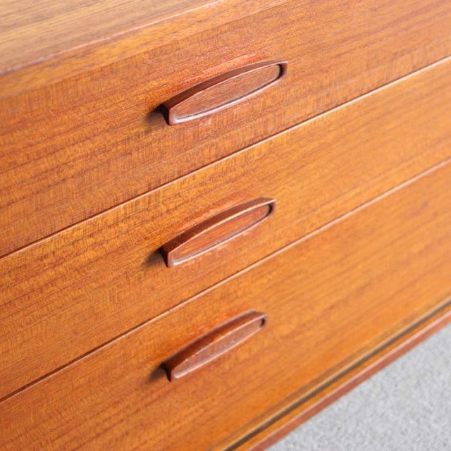 Mid-century British teak sideboard drawers with sleek curved wood handles and rich wood grain detailing.