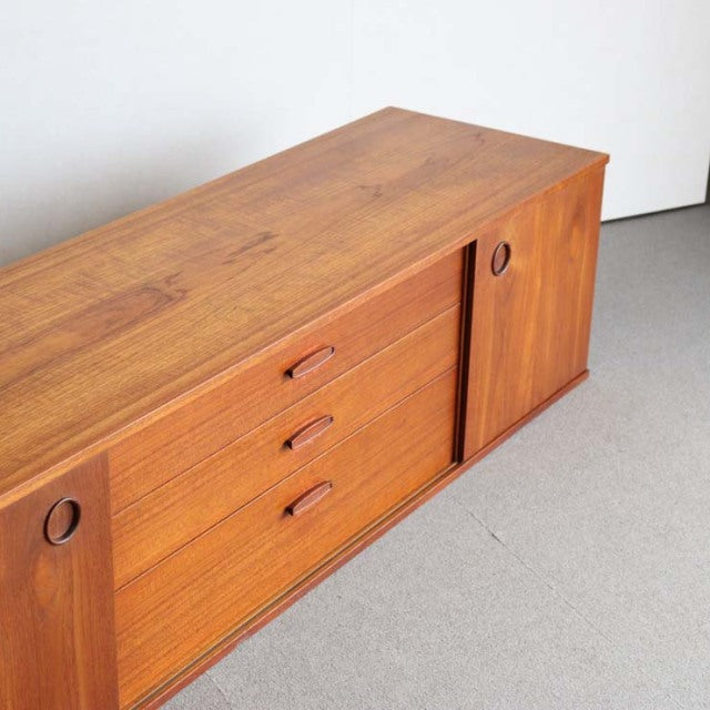 Mid-century vintage teak sideboard by AVALON with smooth wood grain, three drawers, circular recessed handles, and tapered.
