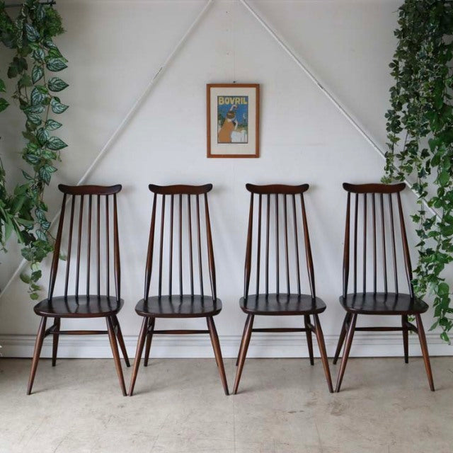 Set of four vintage British Ercol Goldsmith mid-century teak dining chairs with high backs, slender spindle details, and.