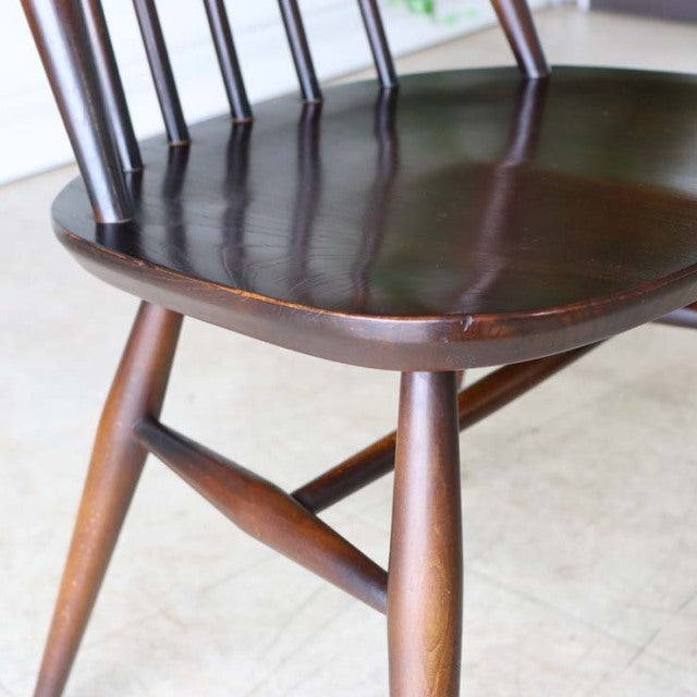 Close-up of a vintage British Ercol Goldsmith mid-century teak dining chair with smooth seat, tapered legs, and visible wood .
