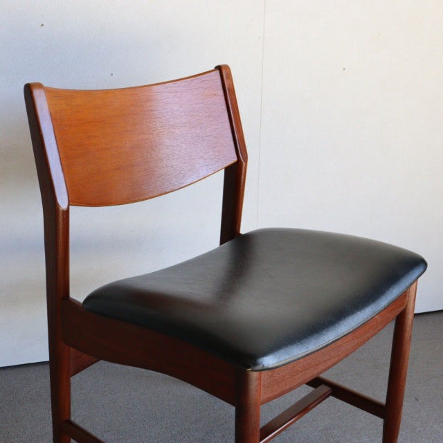 Mid-century British vintage dining chair with teak frame and black leather seat, clean lines and wood grain visible.
