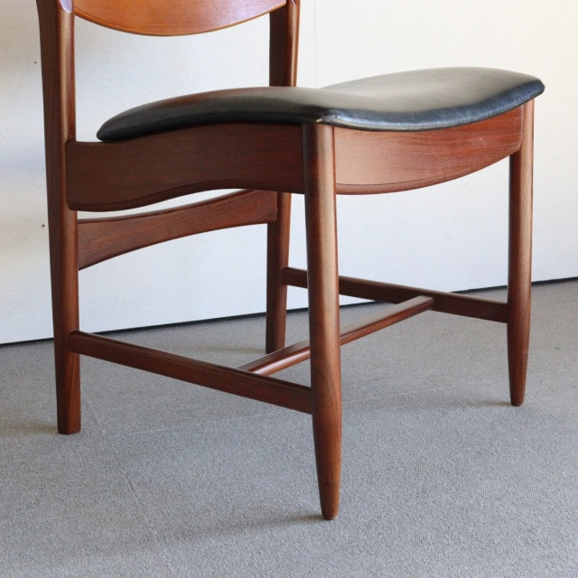 Mid-century British vintage teak dining chair with curved black leather seat and tapered legs.