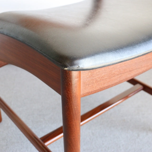 Mid-century British vintage dining chair with smooth teak frame and black leather seat cushion showing fine wood grain and.