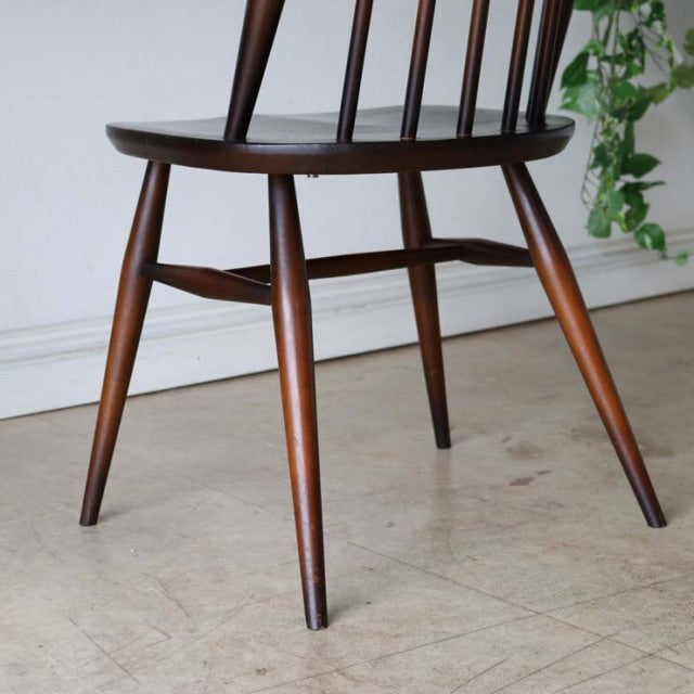 Vintage British mid-century teak dining chair with tapered legs and spindle back, polished wood grain visible.