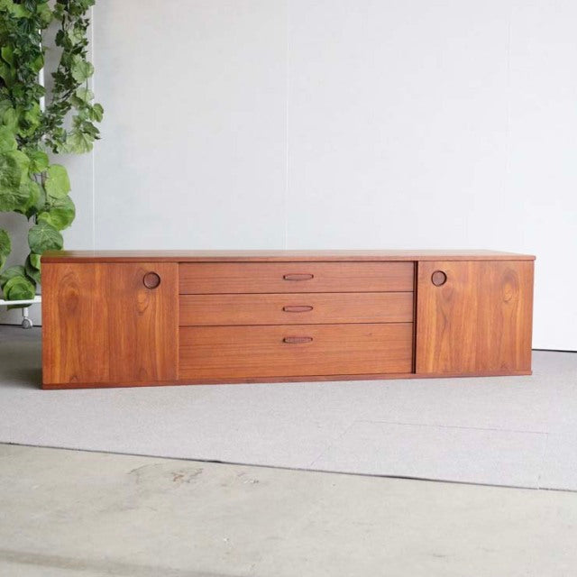 Vintage teak sideboard by AVALON featuring mid-century British-Denmark design, smooth wood grain, rounded wooden handles,.