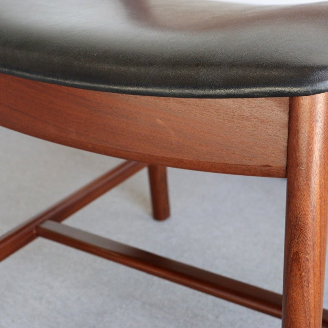 Mid-century British vintage dining chair with teak wood frame and black leather cushioned seat, visible wood grain and.