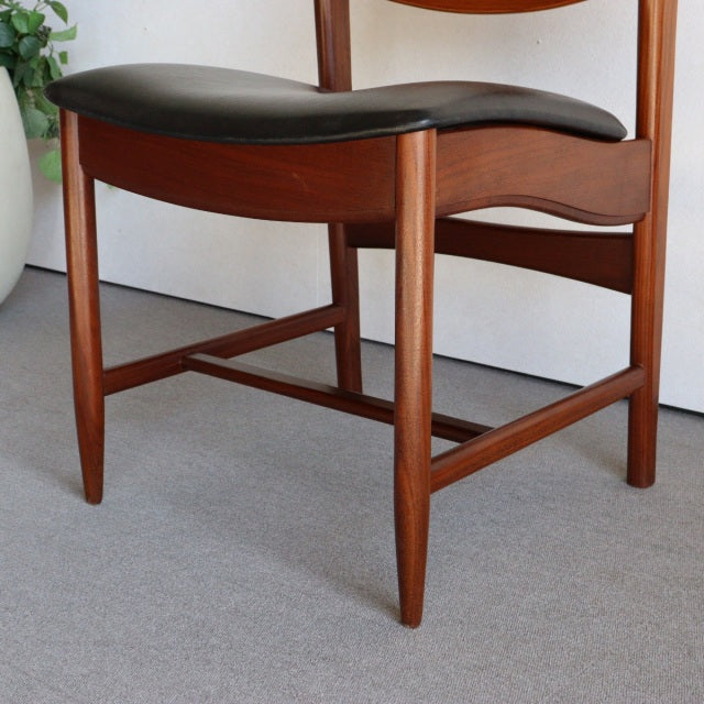 Mid-century vintage British teak stool with gently curved black leather seat and slender tapered legs showing rich wood grain.