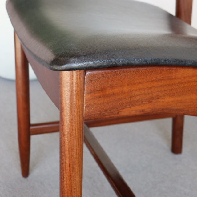 Mid-century British vintage dining chair with teak wood frame and black leather seat, showcasing rich wood grain and tapered .