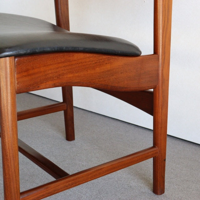Mid-century British vintage dining chair with teak frame, smooth black leather seat, and visible wood grain on legs and.