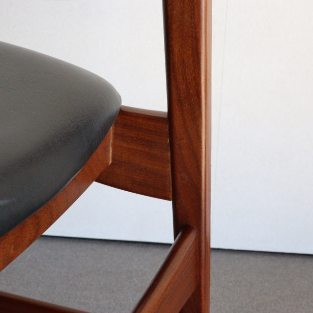 Mid-century British vintage dining chair with rich teak wood frame and smooth black leather seat.