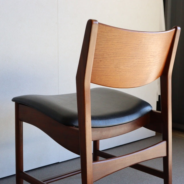Vintage teak British mid-century dining chair with black leather seat, curved wood grain backrest, and sturdy angled legs.
