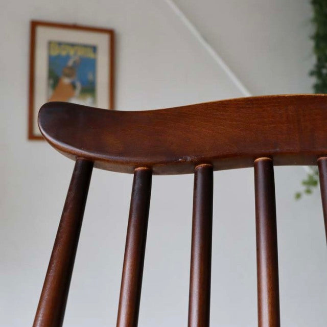 Close-up of vintage British mid-century Ercol Goldsmith teak chair backrest with curved toprail and vertical spindle.